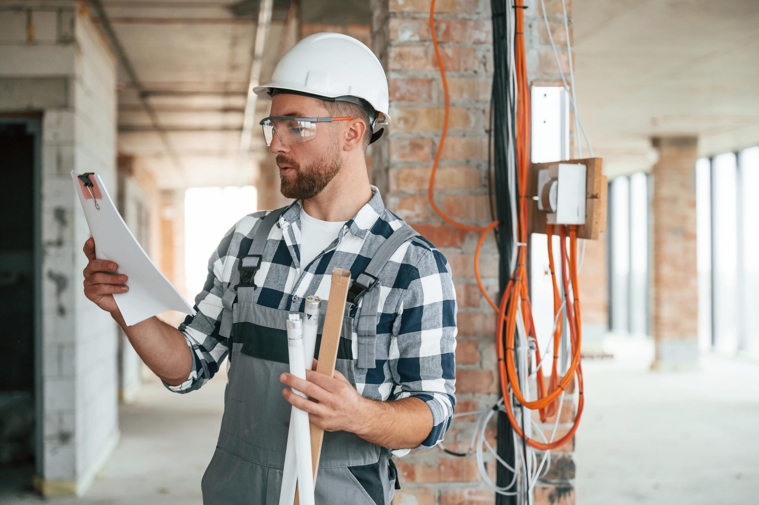An electrician holds fluorescent tubes while reviewing electrical plans.